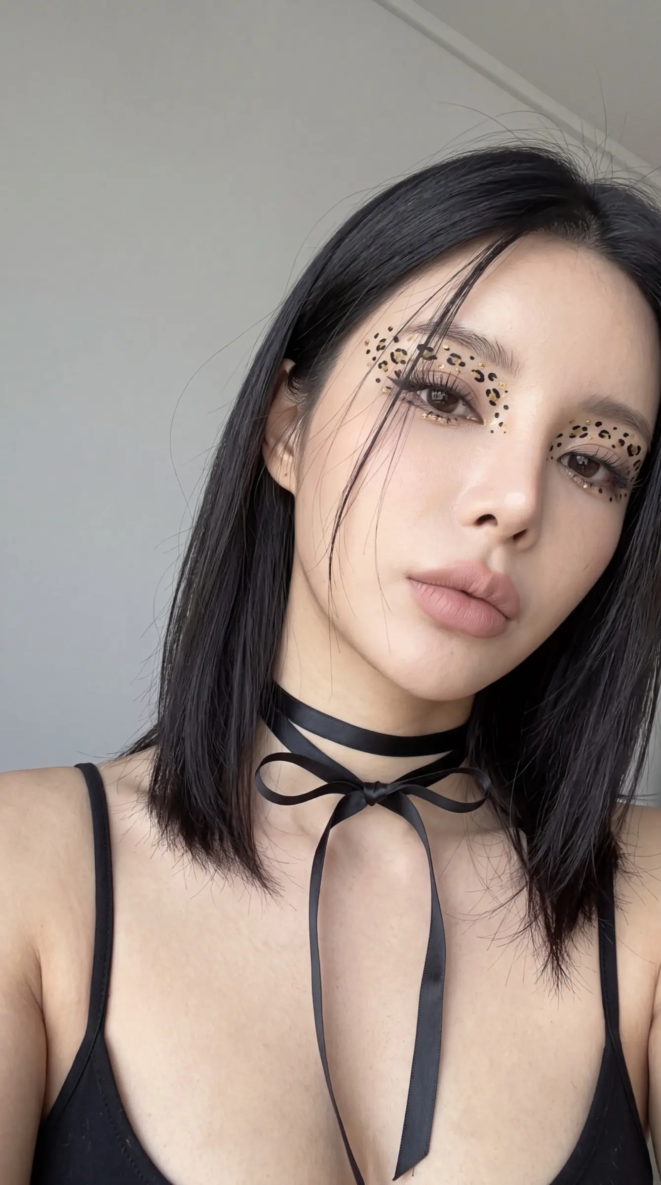 Close selfie of a woman with leopard-spot eye makeup and a black ribbon choker
